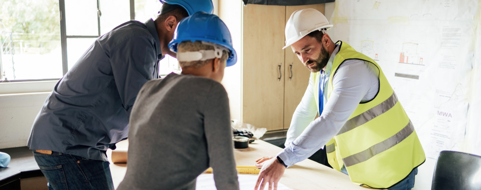 Discussion entre 3 travailleurs au-dessus de plans de construction
